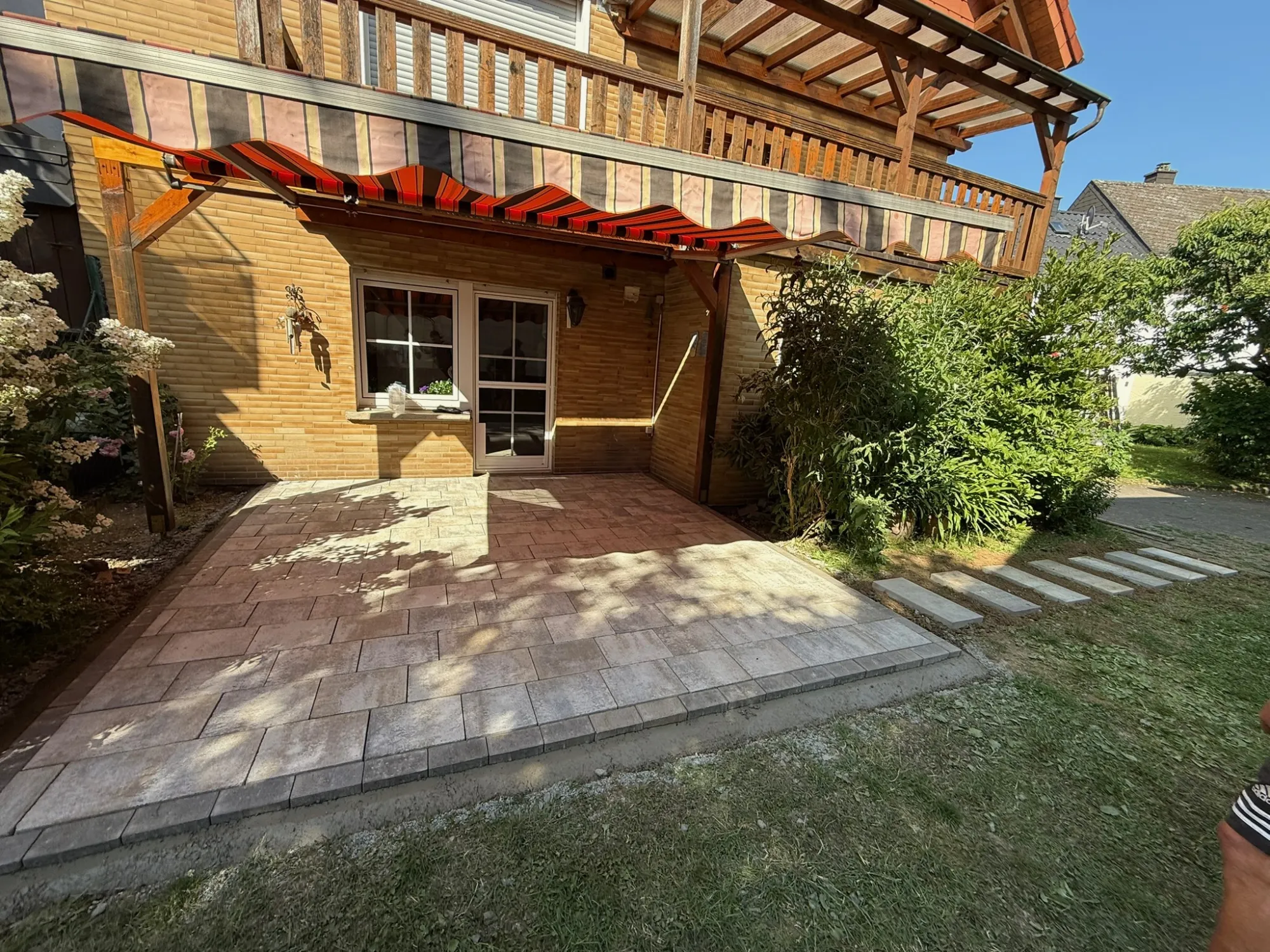 Moderne gepflasterte Terrasse an Wohnhaus mit Holzüberdachung